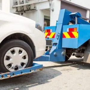Tow truck lifting a white car's wheel.