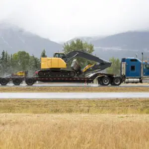 Truck hauling excavator on mountain road.