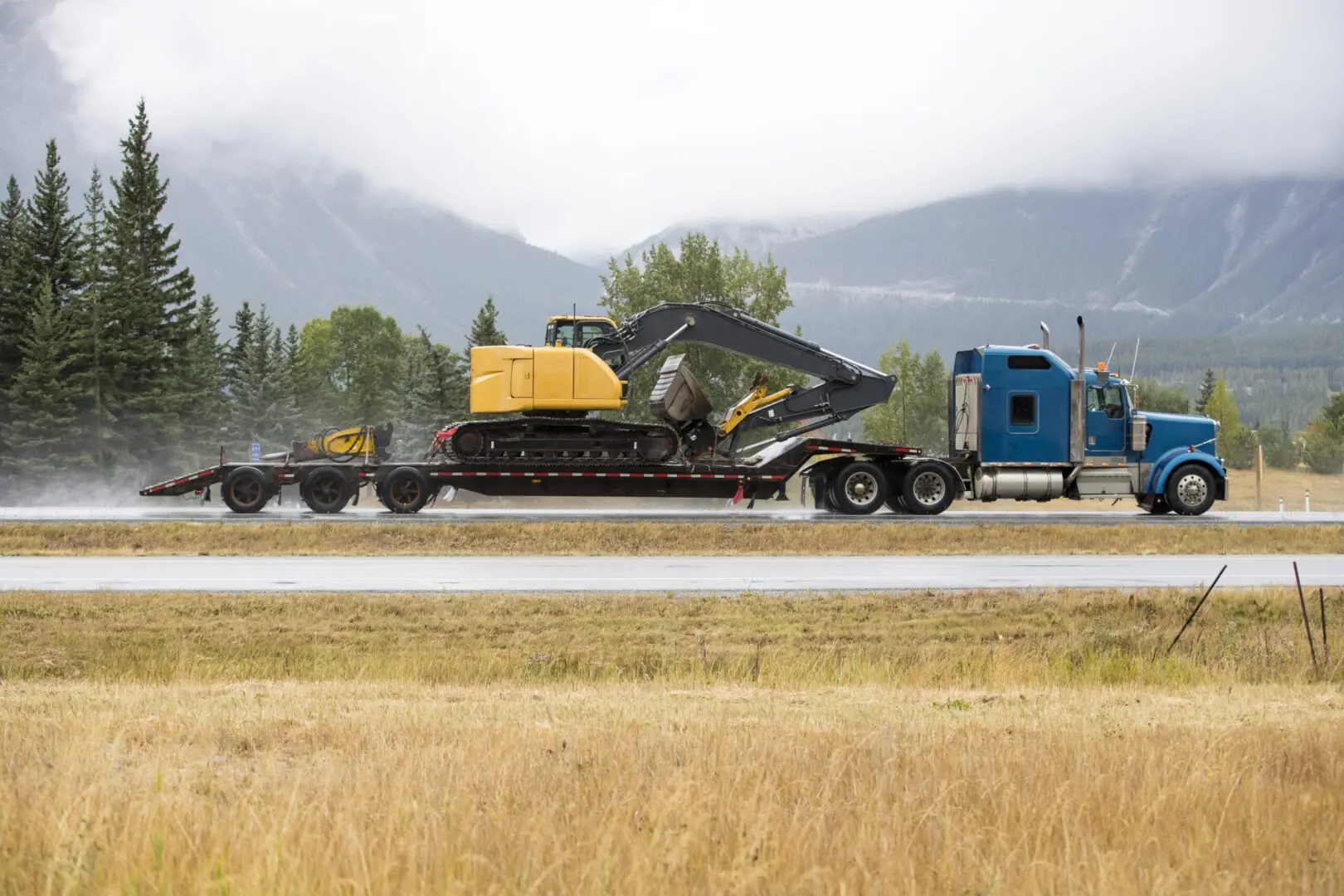 Truck hauling excavator on mountain road.