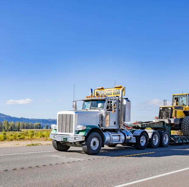 Truck hauling heavy construction equipment on highway.